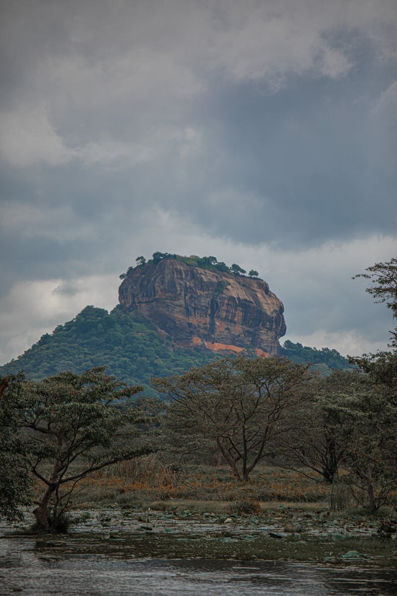 Scenic view of Sigiriya rock fortress amidst lush green nature under cloudy sky in Sri Lanka.