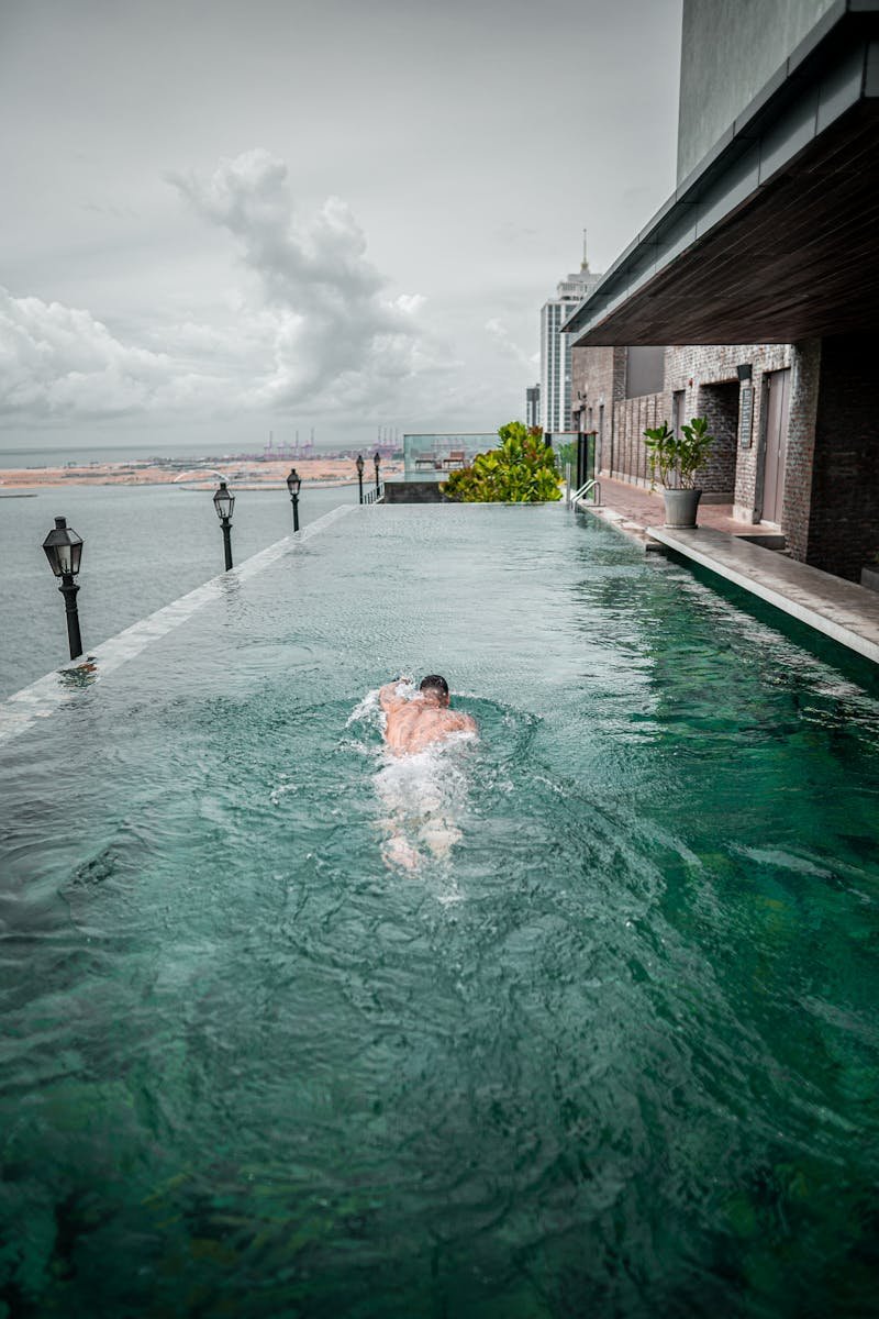 A man swims in an infinity pool on a rooftop with a view of Colombo, Sri Lanka's skyline.